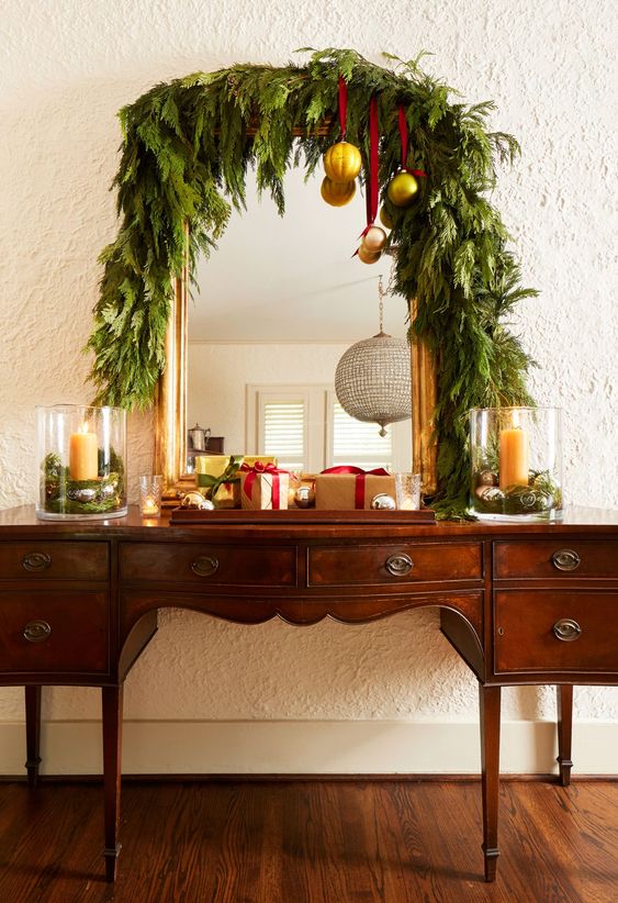 a vintage buffet covered with a lush greenery garland, with gold ornaments on red ribbons plus gift boxes looks very chic