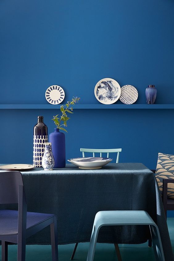 a contemporary dining space with a classic blue wall with a ledge, tuquoise chairs and a grey tablecloth
