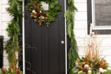 20 a greenery garland covering the doorway, a matching wreath and arrangements in pots with ornaments and pinecones