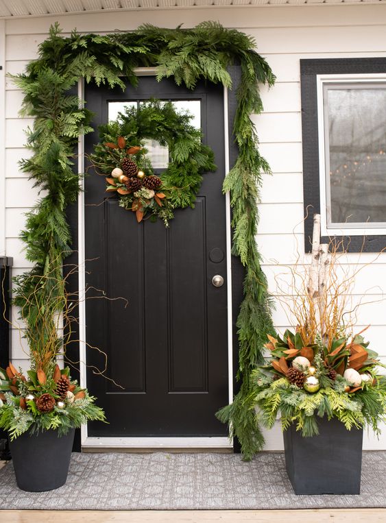 a greenery garland covering the doorway, a matching wreath and arrangements in pots with ornaments and pinecones