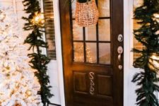 21 a lush evergreen garland with lights over the door, a flocked Christmas tree in a crate and a basket with greenery