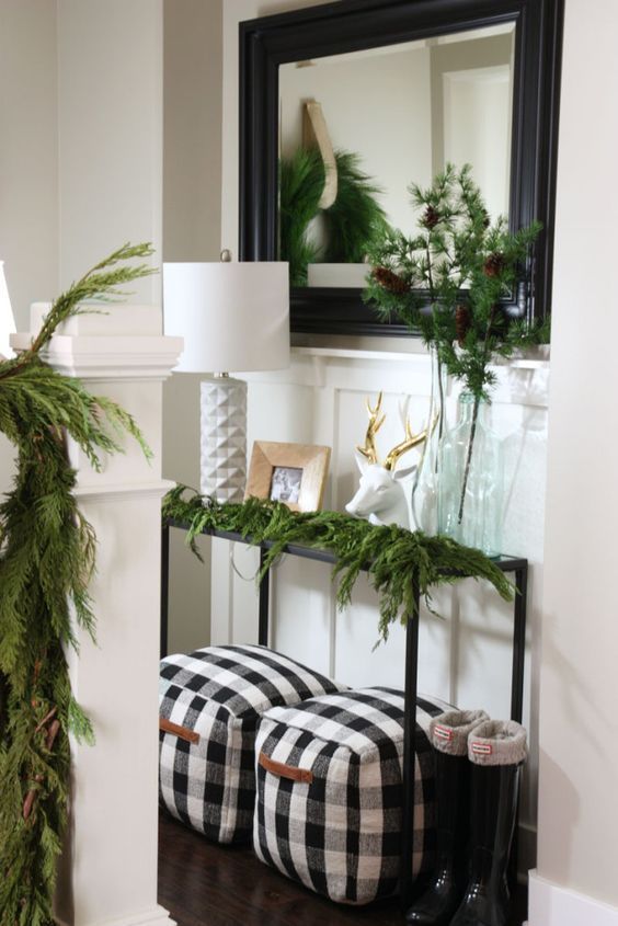 a cozy farmhouse entryway decorated with evergreens and a couple of buffalo check poufs with handles
