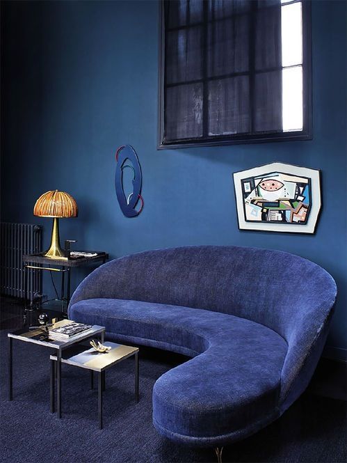 a quirky living room with a classic blue wall, a navy sofa, a cool artwork and some retro touches