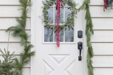 23 a simple evergreen garland covering the doorway, mini Christmas trees in pots and a greenery wreath with a red ribbon bow