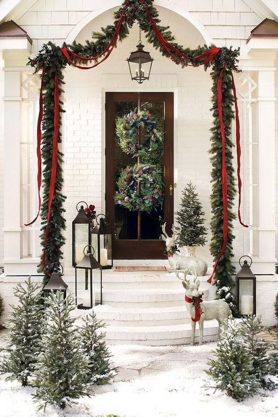 an evergreen garland over the porch with ribbons and bows, evergreen wreaths with pinecones and snowy Christmas trees