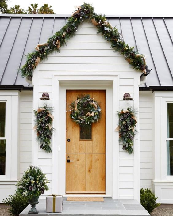 an evergreen garland with pinecones and burlap ribbons covering the porch and posies and wreaths that match