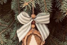 a pretty and all-natural Christmas ornament of a wood slice, wooden beads, a striped bow and a white painted tree is lovely