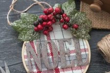 a pretty embroidery hoop Christmas ornament with red and white plaid fabric, glitter letters, snowy leaves and berries for rustic Christmas decor