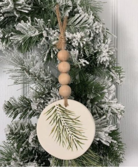 a rustic Christmas ornament of a wood slice with painted evergreens, wooden beads and twine