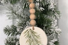 a tree slice Christmas ornament with a painted evergreen branch and some wooden beads is a great rustic decor idea