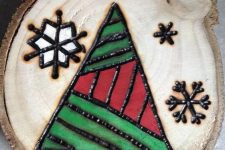 a wood burnt and painted Christmas ornament with snowflakes and a geometric tree
