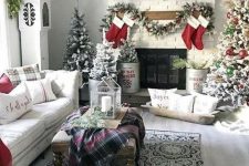 multiple flocked Christmas trees with no decor and red and green ornaments, evergreen garlands and stockings make the space cozy