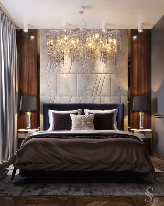 a luxurious bedroom with a stunning chandelier, cool lamps and gorgeous bedding plus a statement headboard