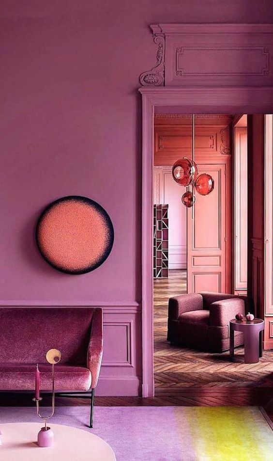 a pink space with molding, an elegant velvet sofa and chic spheric lamps plus parquet floors
