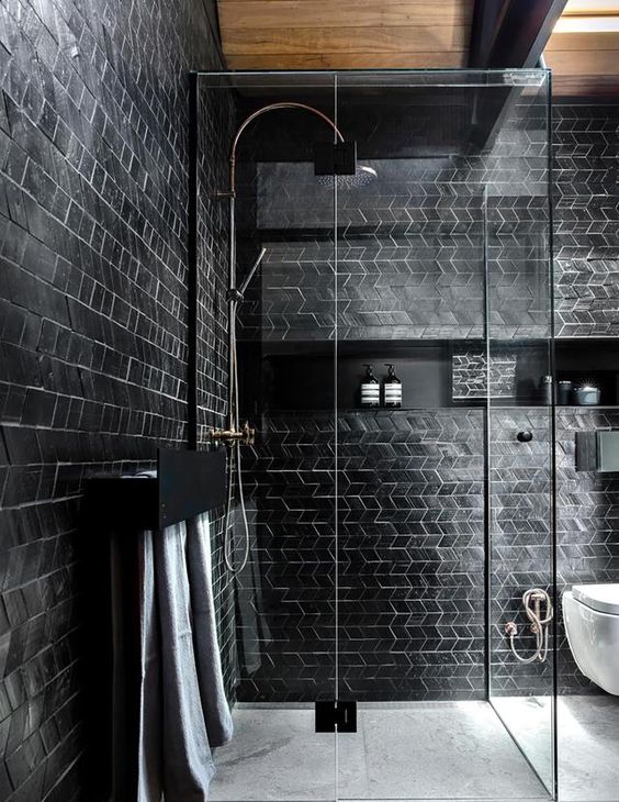 a contemporary bathroom with black tile walls and white grout plus a wooden ceiling