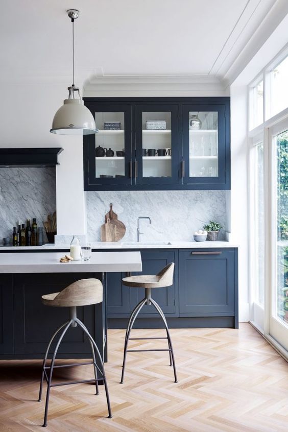 a bold navy kitchen with white countertops and a stone backsplash and pendant lamps is super chic