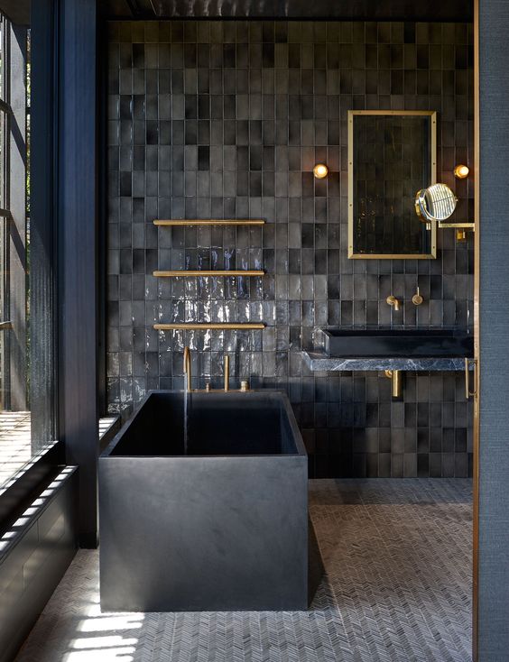 a moody bathroom done in greys and black, with elegant brass fixtures and a glazed wall