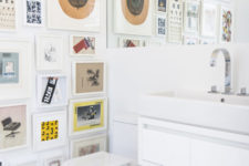07 The powder room is done with a colorful gallery wall, sleke white appliances and a large mirror