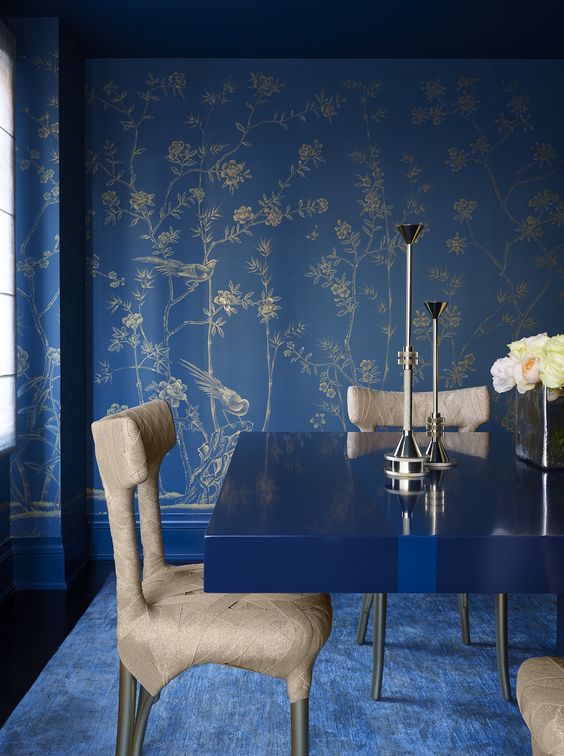 a bright blue living room with botanical printed wallpaper, a modern table and wrapped chairs