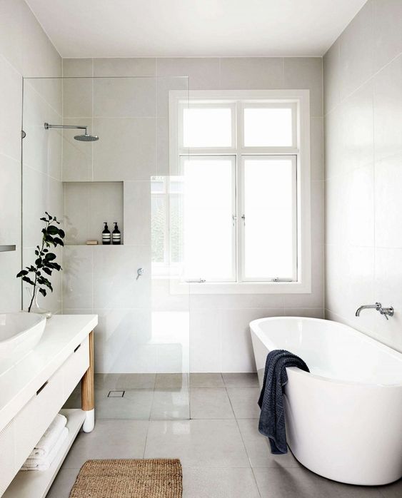 a clean and neutral minimalist bathroom done with neutral tiles and a white vanity and bathtub