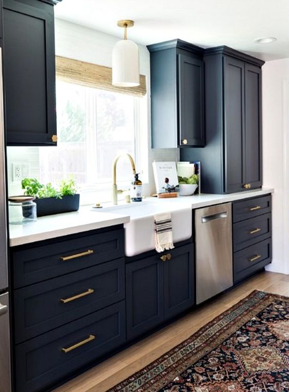 a stylish navy kitchen with gold fixtures and handles, a white countertop and chic lamps