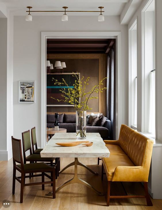 A chic dining room with a stone slab table, leather chairs and a large amber colored leather bench