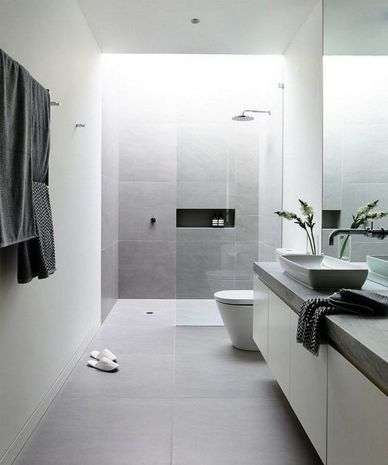 a clean minimalist bathroom done with white concrete and grey tile walls plus stone countertops