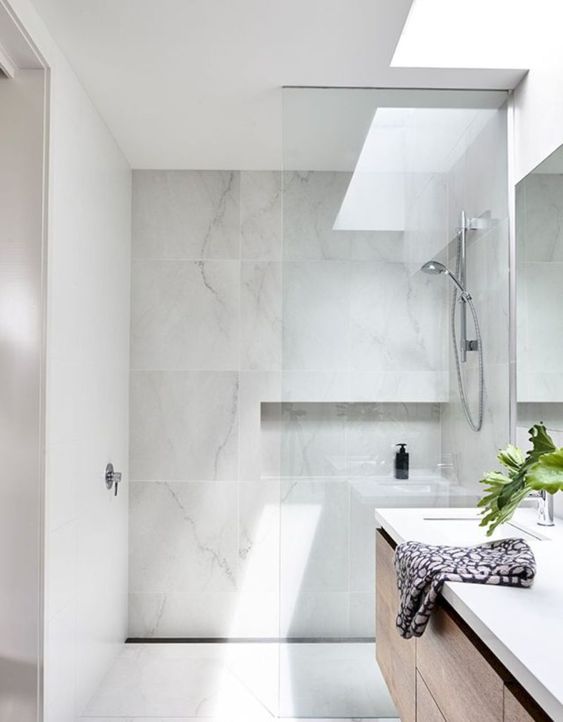 a chic and clean minimalist bathroom done with white marble tiles and a skylight to make the space more welcoming