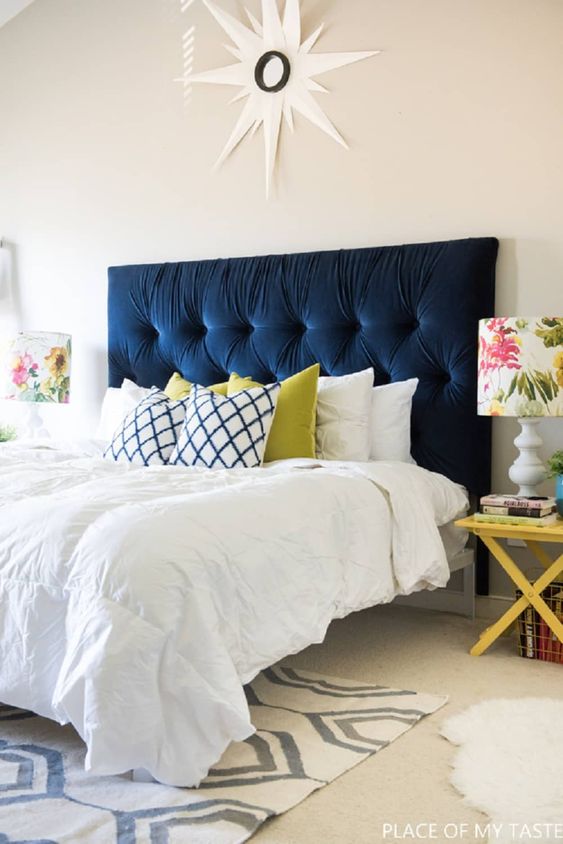 a navy tufted headboard is the main centerpiece of the bedroom, it brings color and makes a statement