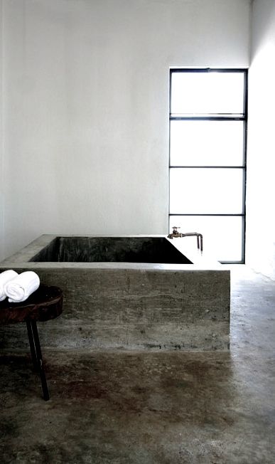 an ultra-minimalist bathroom done in concrete with a large soaking bathtub and white concrete walls