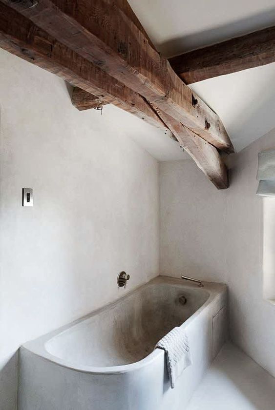 a concrete bathroom with white walls and a grey bathtub plus wooden beams on the ceiling