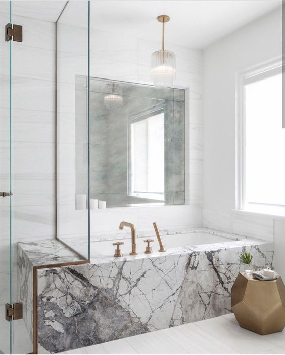 a neutral bathroom with a unique marble clad bathtub and brass fixtures for a more chic look