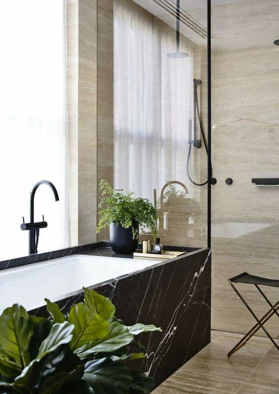 a black marble clad bathtub stands out a lot in a neutral warm-colored space