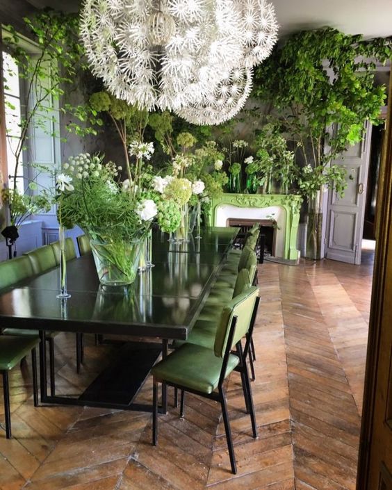 a refined dining room refreshed with a green fireplace and chairs and lots of greenery arrangements in vases and pots