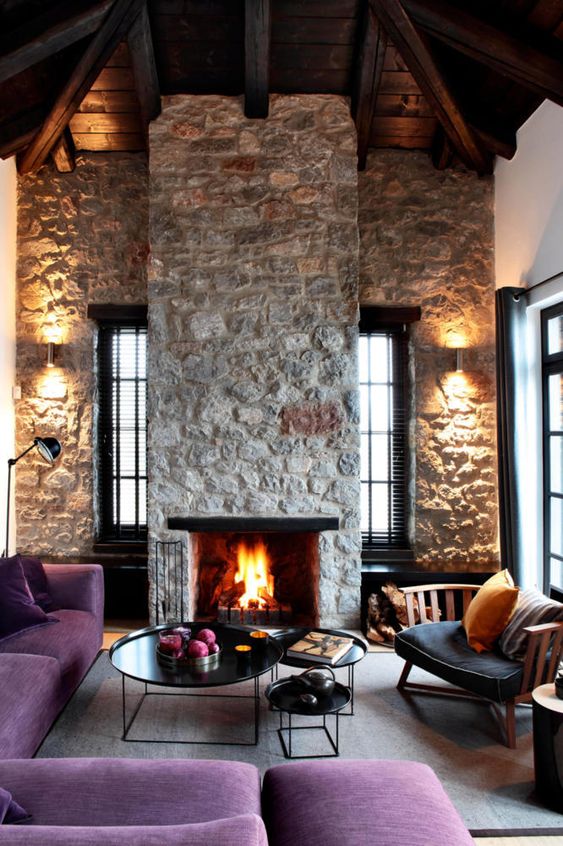 a bright contemporary living room with rough stone walls and a fireplace, purple furniture and elegant round tables