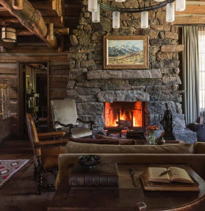 A cabin style living room done with lots of rough wood, a large stone hearth and vintage furniture of wood and leather