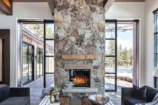 a chic contemporary cabin space with dark furniture, wood slab tables and a spectacular stone fireplace with a wooden mantel