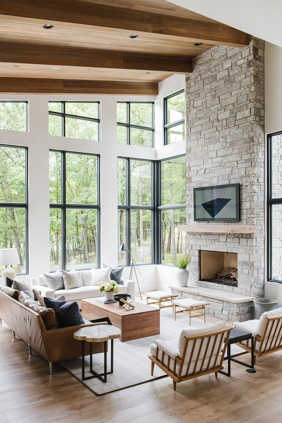 A clean and modern double height living room with a grey stone fireplace and a wooden mantel as a centerpiece