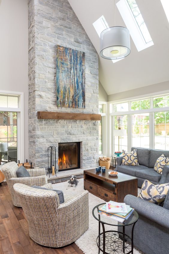 A clean double height neutral living room with a grey stone fireplace with a wooden mantel and a bright blue artwork