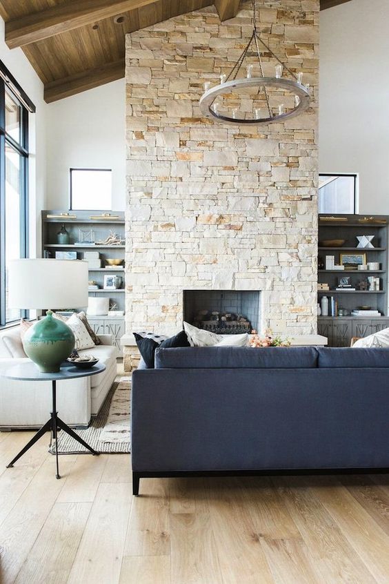A contemporary living room in neutrals, with a double height ceiling, a stone fireplace that warms up the space