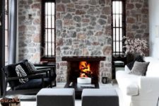 a contemporary monochromatic space with bright stone walls and a fireplace, elegant and laconic black and white furniture