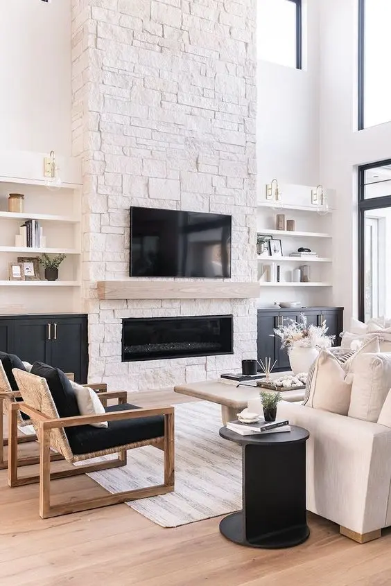 A contrasting living room with a stone fireplace, shelves and built in cabinets, a white sofa, black chairs, a black side table