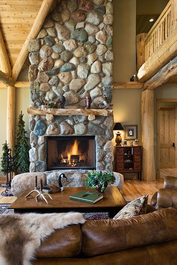 a gorgeous cabin space with a large scale stone fireplace with rocks at its base, leather and wood furniture