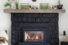a large black stone clad fireplace with a wooden mantel is a great cabin or woodland touch to the space