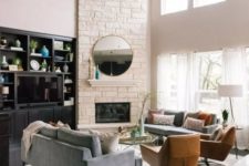 a stylish modern living room with a white faux stone corner fireplace with a small mantel, a round mirror and double-height windows