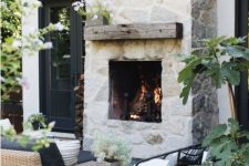 a whitewashed stone fireplace with a rough wooden mantel is a centerpiece of this chic outdoor space
