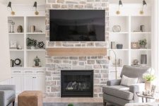 a whitewashed stone fireplace with a wooden mantel and storage units on each side of it is a cozy and chic touch to the room decor