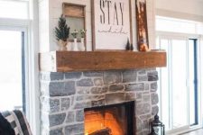 a whitewashed stone fireplace with lanterns by its side, a wooden mantel with artworks and potted plants