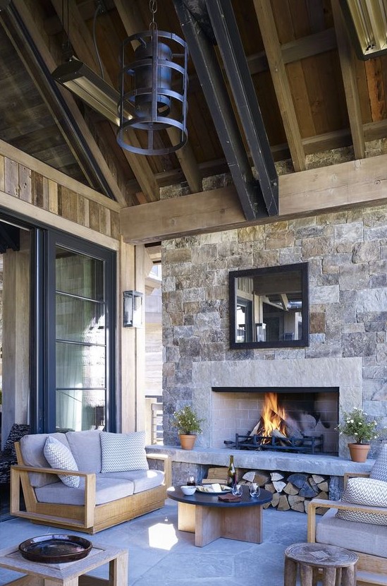 an outdoor space under a roof, with a stone fireplace, neutral modern furniture, metal pendant lamps and a low coffee table is chic