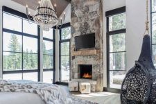 an ultra-modern chalet bedroom with a stone fireplace, a suspended chair, a catchy chandelier and lots of faux fur